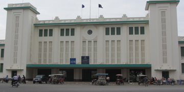 Gare historique de Phnom Penh, avec son architecture Art déco caractéristique, son horloge centrale, ses touches de vert et une rue animée devant le bâtiment.