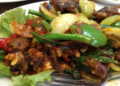 Cambodian stir-fried eels with spices, green beans, peppers, onions, garlic, and fresh herbs on a plate.