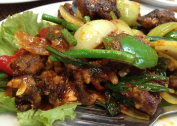 Cambodian stir-fried eels with spices, green beans, peppers, onions, garlic, and fresh herbs on a plate.