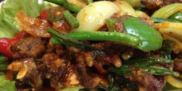 Cambodian stir-fried eels with spices, green beans, peppers, onions, garlic, and fresh herbs on a plate.