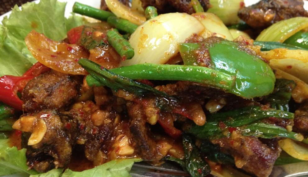 Cambodian stir-fried eels with spices, green beans, peppers, onions, garlic, and fresh herbs on a plate.