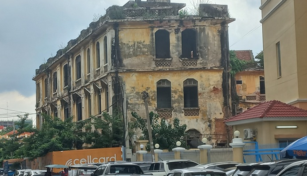 Old colonial-era commissariat building near Wat Phnom in Phnom Penh, Cambodia, with weathered yellow walls overlooking a busy street.