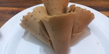 Golden Cambodian thâng muon wafers with black sesame seeds arranged on a white plate.
