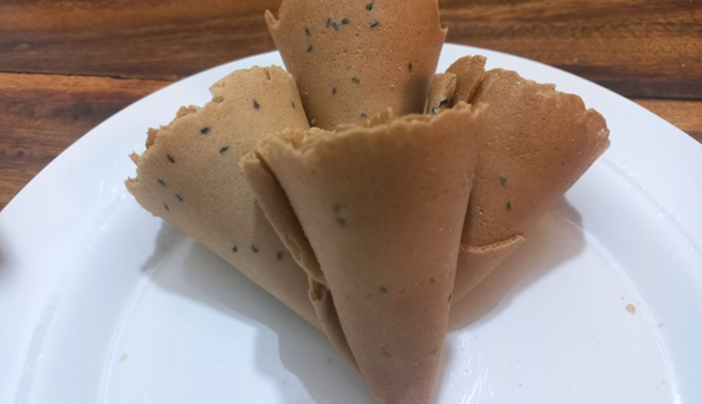Golden Cambodian thâng muon wafers with black sesame seeds arranged on a white plate.