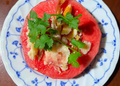 Cambodian hot-season dish of sliced watermelon topped with grilled dried fish, herbs, and spices on a blue-and-white plate.