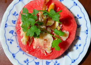 Cambodian hot-season dish of sliced watermelon topped with grilled dried fish, herbs, and spices on a blue-and-white plate.
