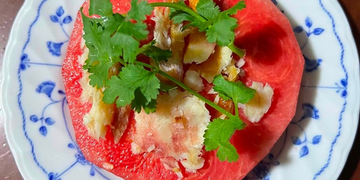 Cambodian hot-season dish of sliced watermelon topped with grilled dried fish, herbs, and spices on a blue-and-white plate.