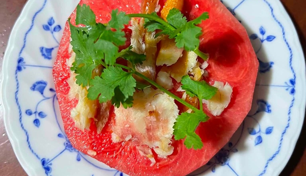 Cambodian hot-season dish of sliced watermelon topped with grilled dried fish, herbs, and spices on a blue-and-white plate.